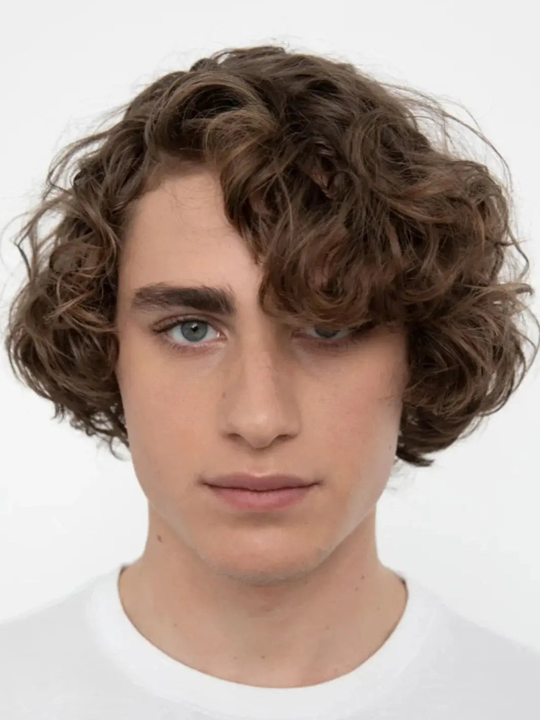 A close-up headshot of a model showcasing soft, textured curls styled using R+Co TURNTABLE Curl Defining Cream | Twentyseven Toronto