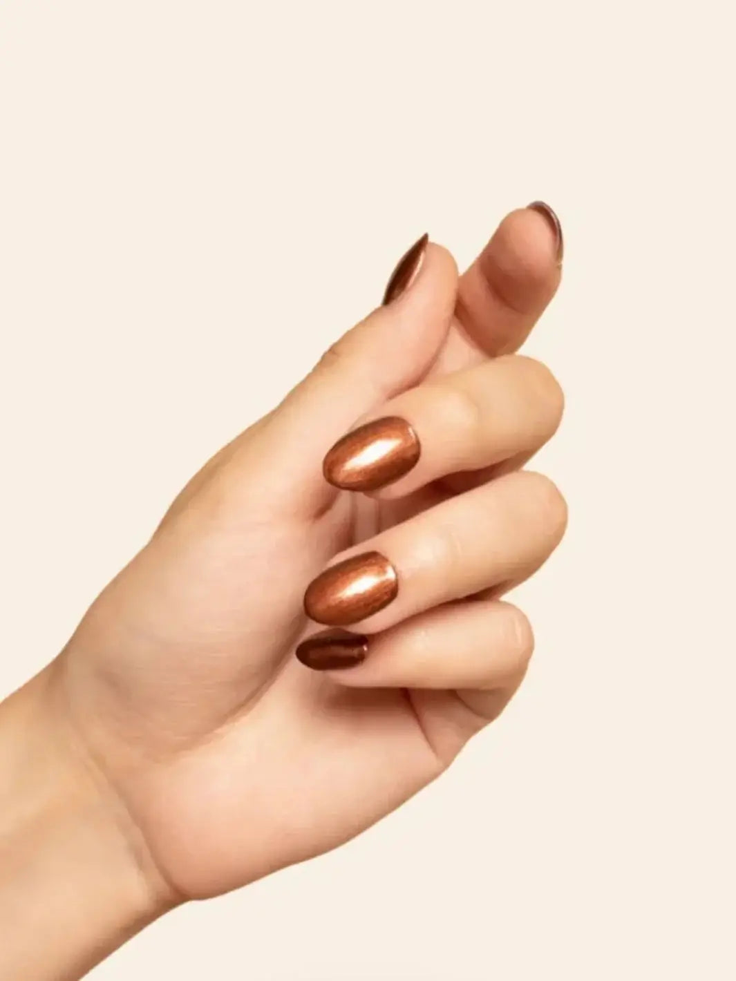 A hand with a neat manicure showcases the metallic, metallic-copper finish of BKIND Nail Polish in Une Cenne against an off-white background | Twentyseven Toronto