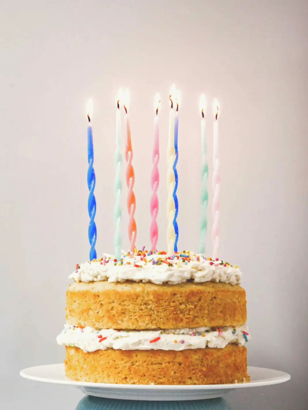 A two-layered cake made from the Glazed Cake Co Vanilla Bean signature kit features fluffy white frosting, colorful sprinkles, and seven lit, spiral birthday candles | Twentyseven Toronto