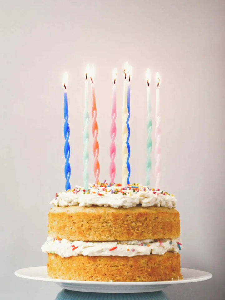 A two-layered cake made from the Glazed Cake Co Vanilla Bean signature kit features fluffy white frosting, colorful sprinkles, and seven lit, spiral birthday candles | Twentyseven Toronto