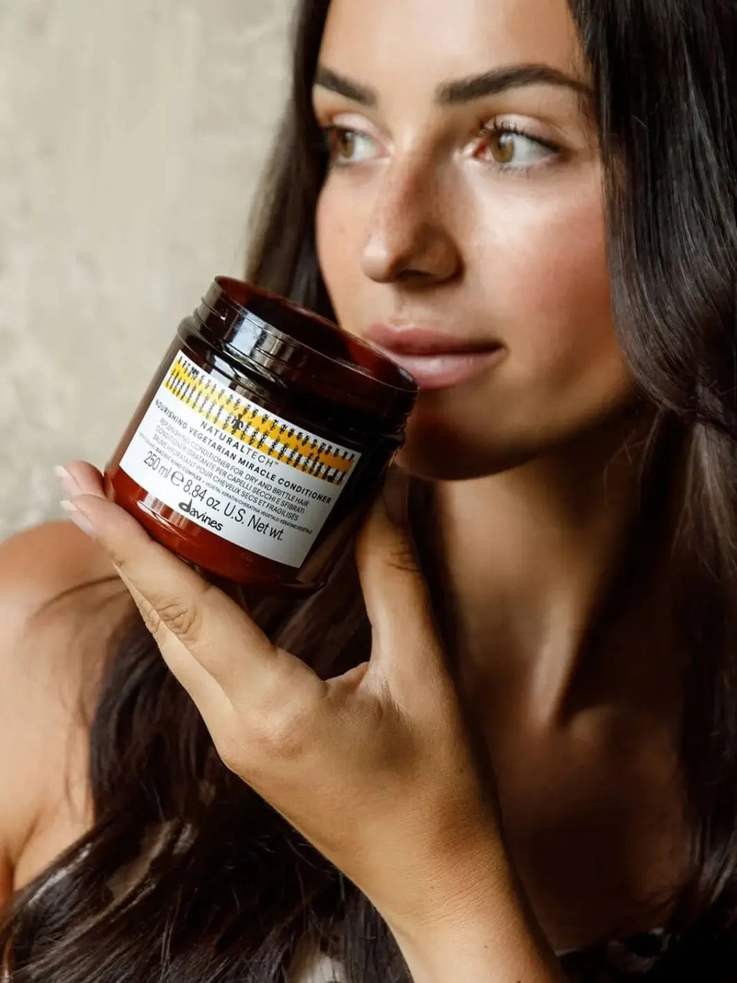 A close-up shot shows a woman holding a jar of Davines NOURISHING Vegetarian Miracle Conditioner near her face | Twentyseven Toronto