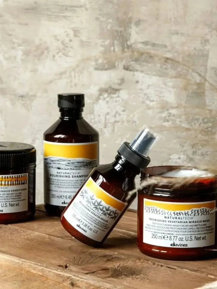 A jar of Davines NOURISHING Vegetarian Miracle Conditioner sits on a wooden shelf next to matching bottles of shampoo, keratin sealer, and a hair mask | Twentyseven Toronto