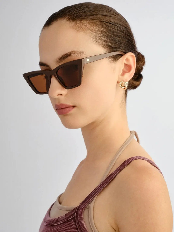 A side-angle profile of a woman showcasing the thick temple arm and tiny gold logo detail of the Le Specs Velodrome - Cocoa sunglasses | Twentyseven Toronto