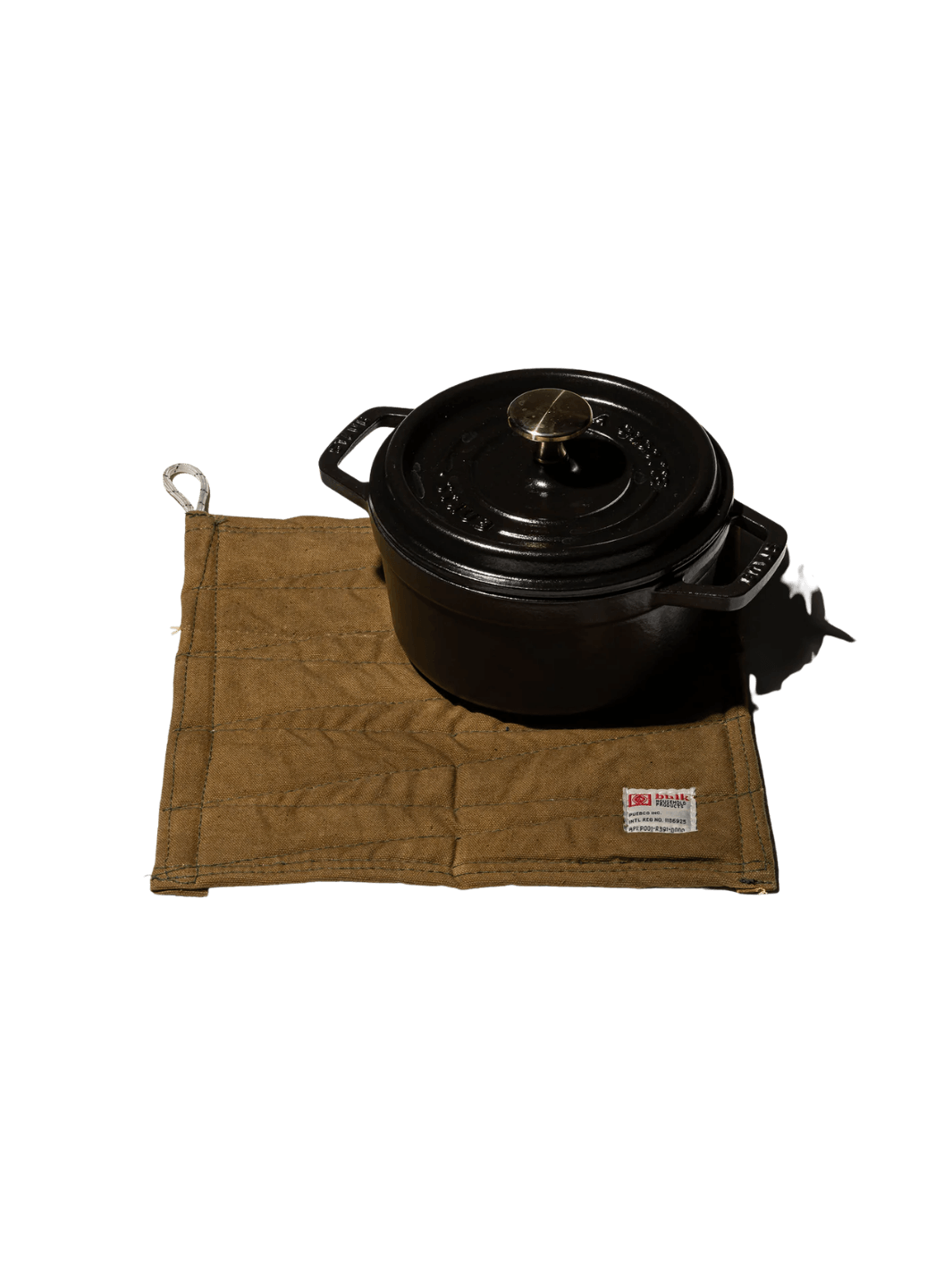 A heavy black cast-iron pot rests on top of a tan canvas Vintage Bivouac Trivet from Puebco against a transparent background | Twentyseven Toronto