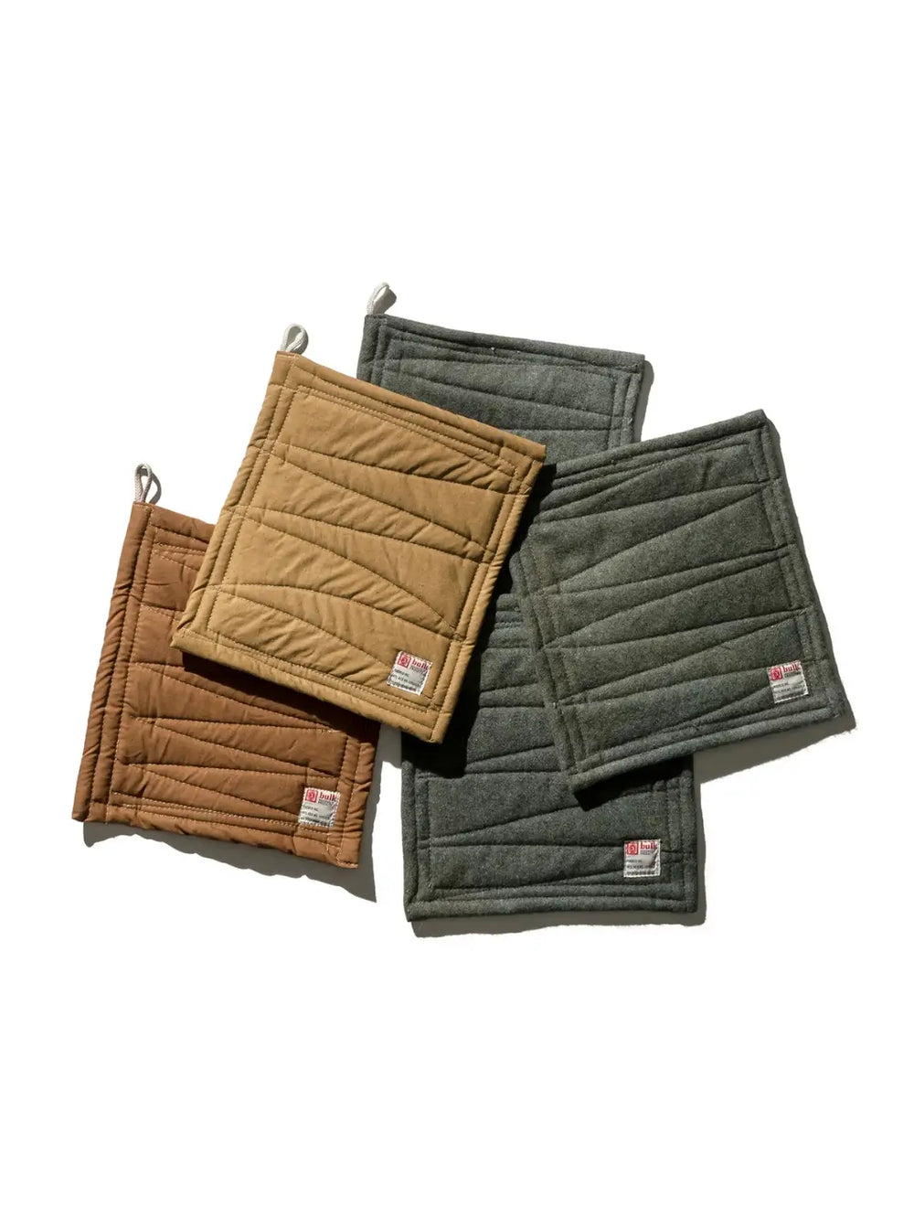 An assortment of Vintage Bivouac Trivet from Puebco fabric pot holders in tan, brown, and grey are scattered across a white surface | Twentyseven Toronto