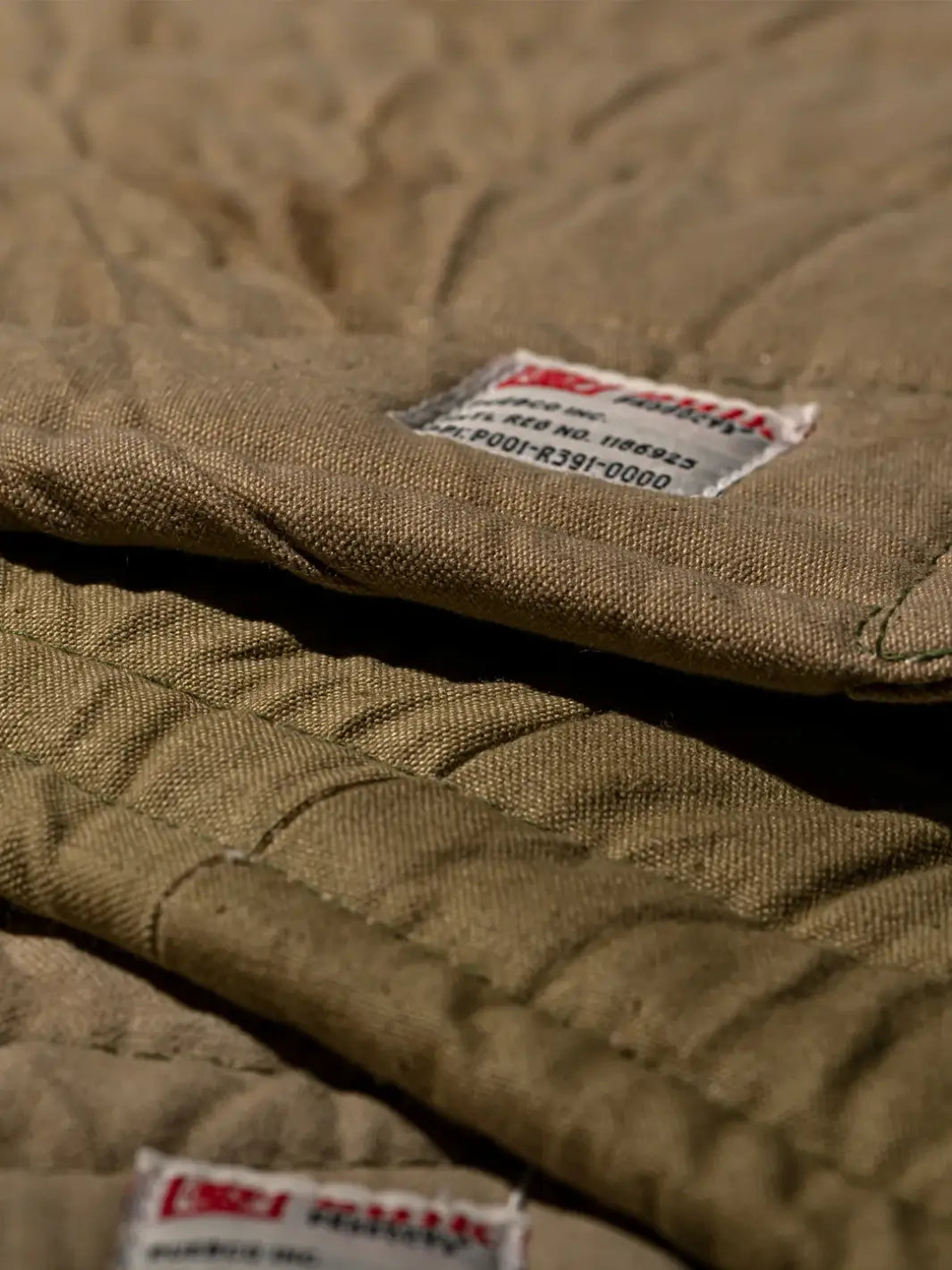 A close-up shot highlights the heavy canvas texture and white branded fabric label on a brown Vintage Bivouac Trivet from Puebco | Twentyseven Toronto