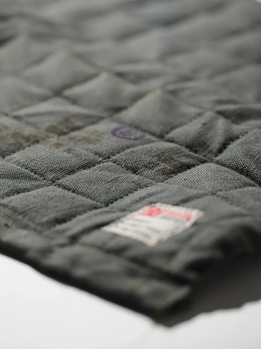 A close-up shot details the grid-quilted stitching and rugged, weathered texture of a grey Vintage Bivouac Trivet from Puebco | Twentyseven Toronto