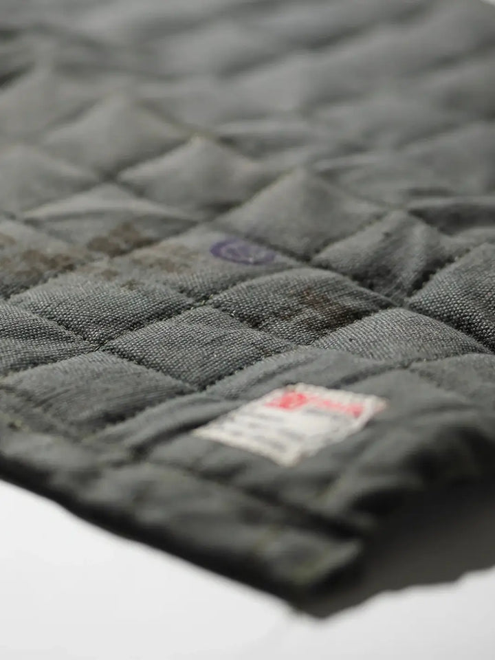 A close-up shot details the grid-quilted stitching and rugged, weathered texture of a grey Vintage Bivouac Trivet from Puebco | Twentyseven Toronto