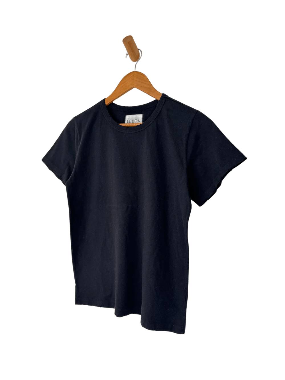The Le Bon Shoppe Vintage Boy Tee - True Black is displayed hanging from a wooden wall peg against a transparent background | Twentyseven Toronto