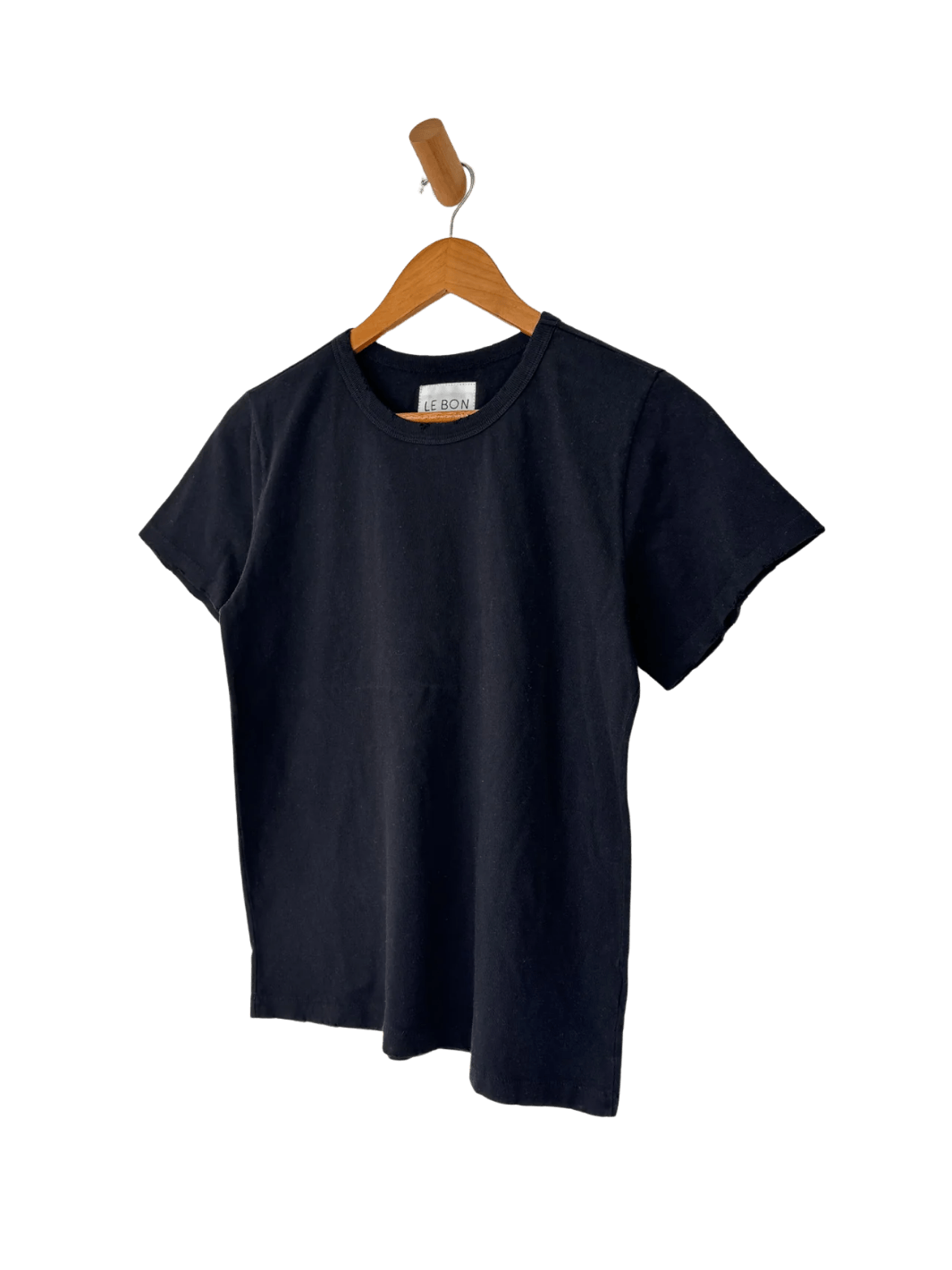 The Le Bon Shoppe Vintage Boy Tee - True Black is displayed hanging from a wooden wall peg against a transparent background | Twentyseven Toronto