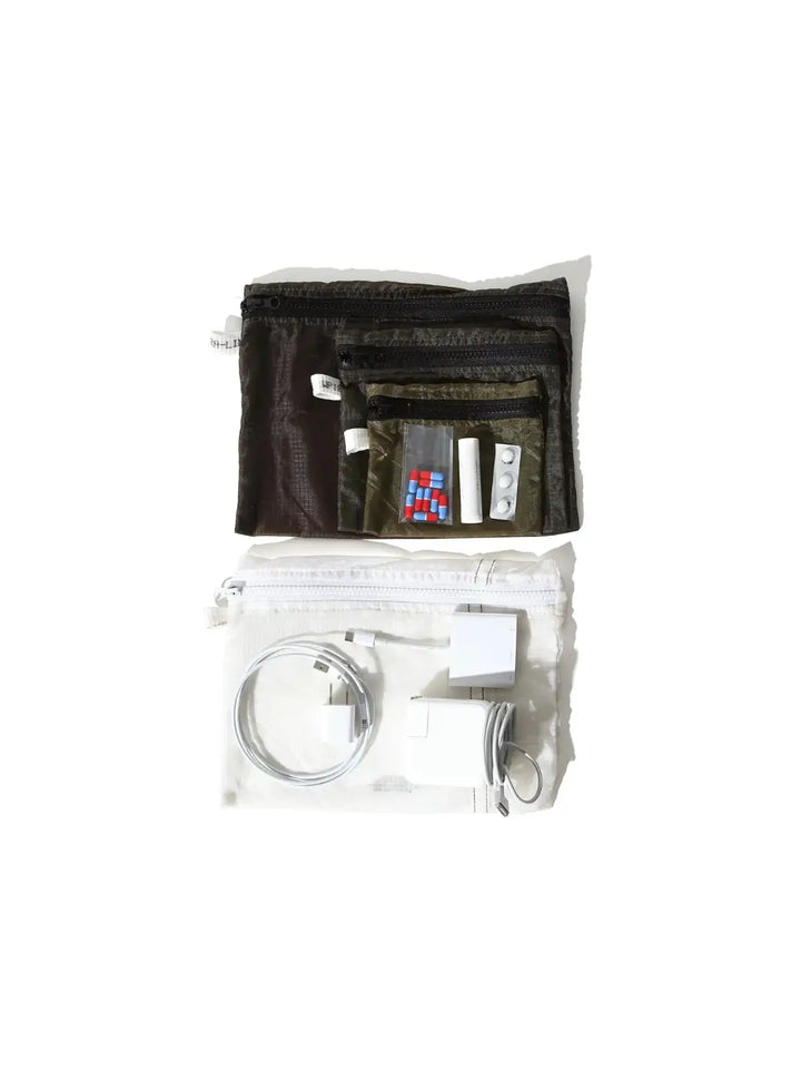 Everyday travel essentials, including charging blocks and medication organized inside and around the semi-translucent, white Vintage Parachute Light Pouch Medium from Puebco alongside a nested set of smaller olive-green pouches | Twentyseven Toronto
