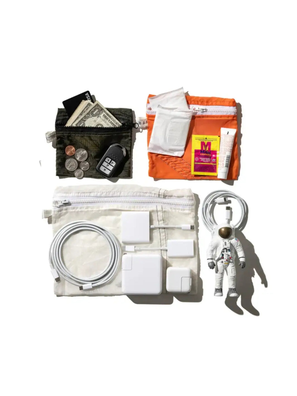 A top-down flat lay displays everyday items organized in Vintage Parachute Light Pouches from Puebco alongside an astronaut figurine, personal care items on an orange pouch, and cash and keys on a dark green pouch | Twentyseven Toronto