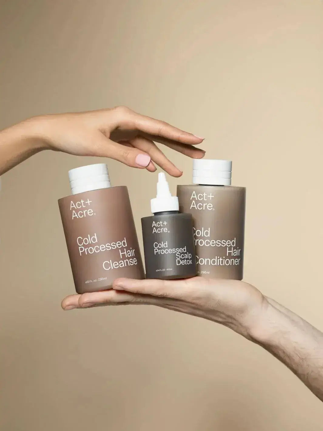 Three bottles of Act+Acre hair care products held by hands against a beige background | Twentyseven Toronto