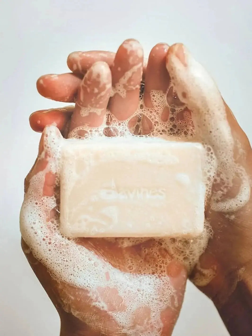 A pair of hands covered in rich white lather holds an unwrapped solid bar, showing how the Davines VOLU Shampoo Bar suds up during use | Twentyseven Toronto
