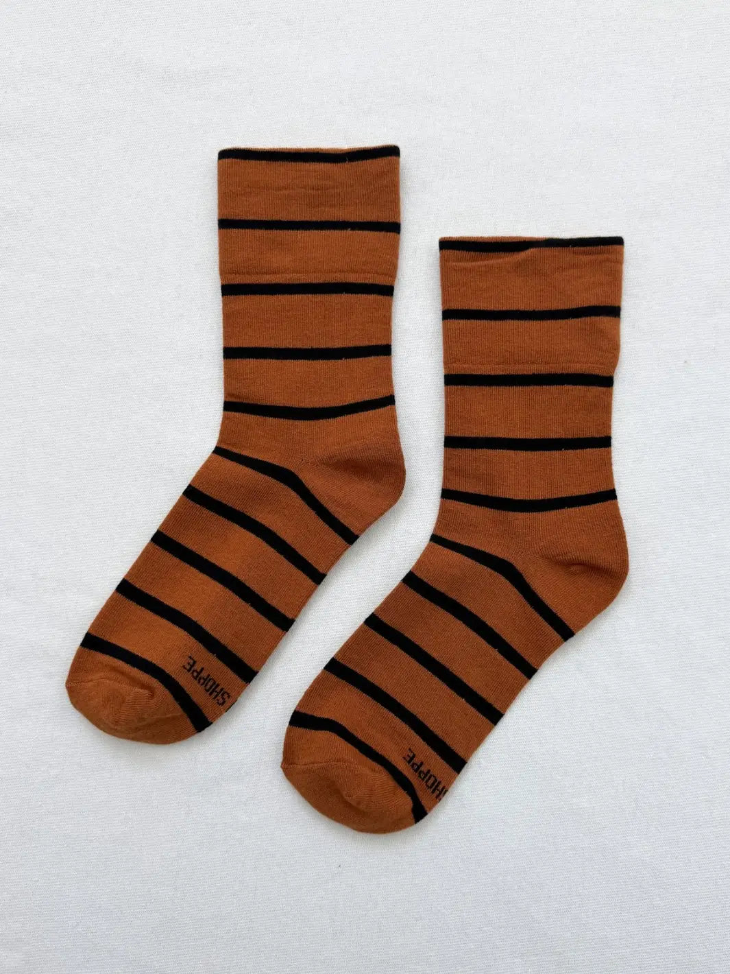 A pair of copper-brown and black striped Wally Socks in Camel from Le Bon Shoppe is laid flat against a clean white backdrop | Twentyseven Toronto