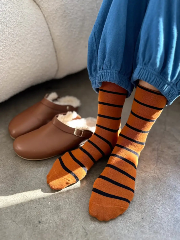 A person wearing blue sweatpants showcases the striped Wally Socks in Camel from Le Bon Shoppe next to a pair of brown leather, fleece-lined clogs | Twentyseven Toronto