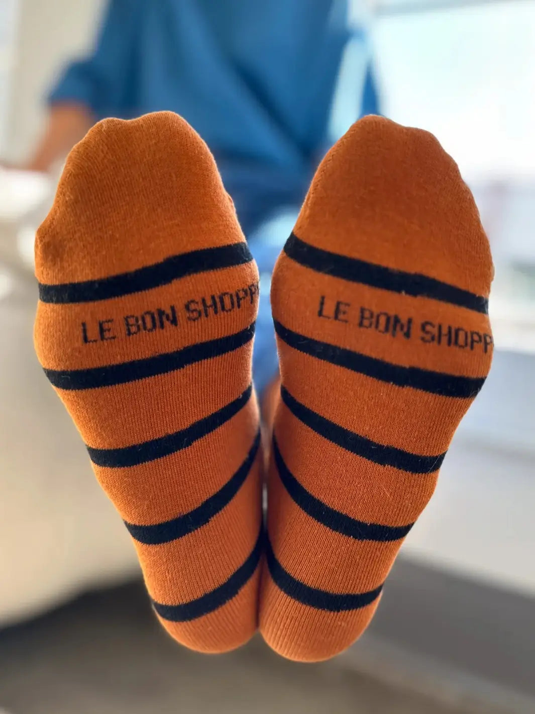 The soles of the orange striped Wally Socks in Camel from Le Bon Shoppe are held up to clearly display the black knit "LE BON SHOPPE" text | Twentyseven Toronto