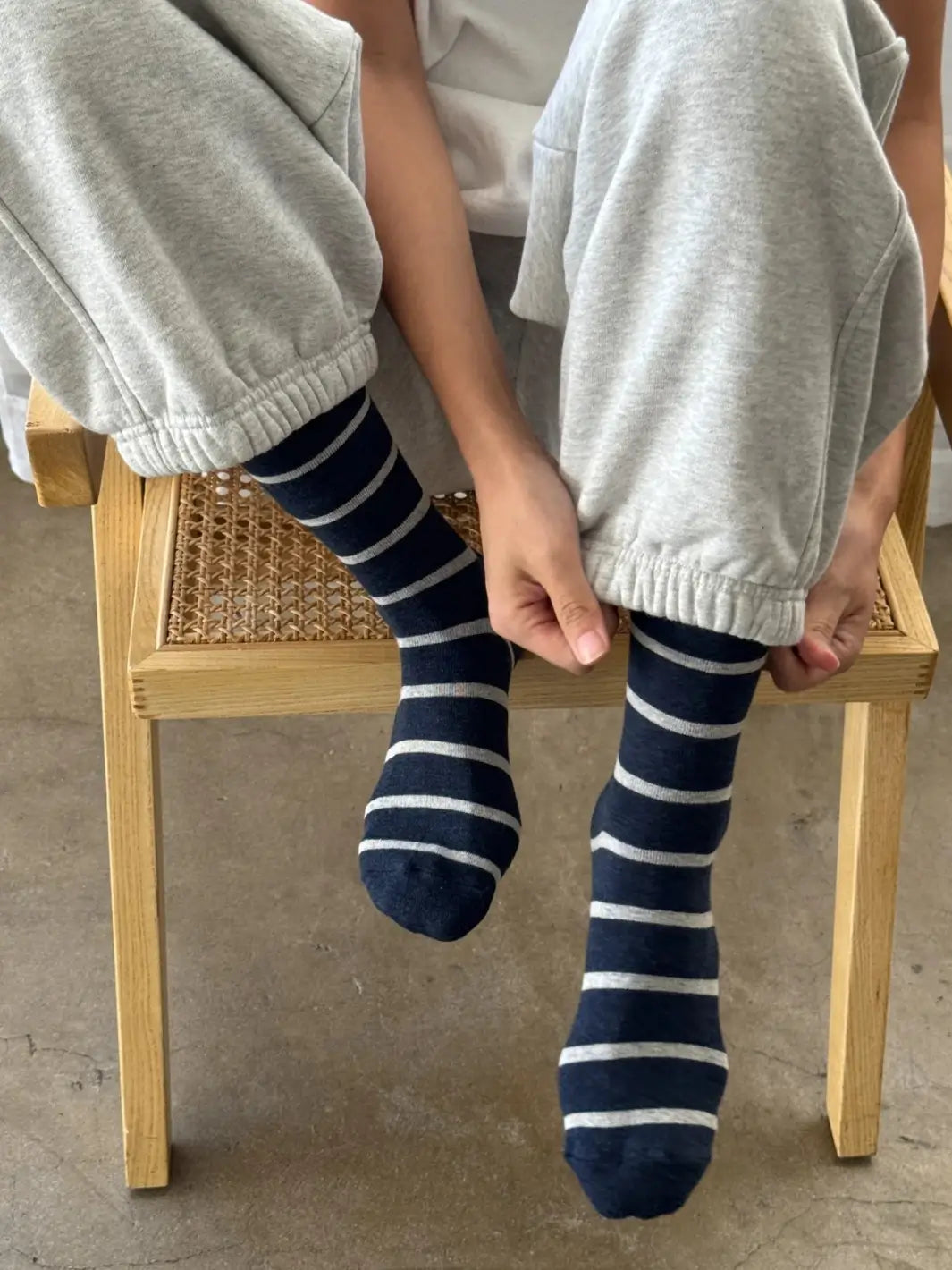 A person sitting on a woven chair adjusts their gray sweatpants to show off their striped Wally Socks in Marine from Le Bon Shoppe | Twentyseven Toronto