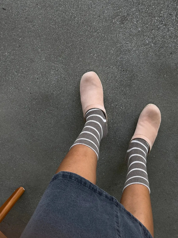 A top-down view shows a person wearing the striped Wally Socks in Mocha from Le Bon Shoppe styled with pale pink slip-on clogs and a denim skirt | Twentyseven Toronto