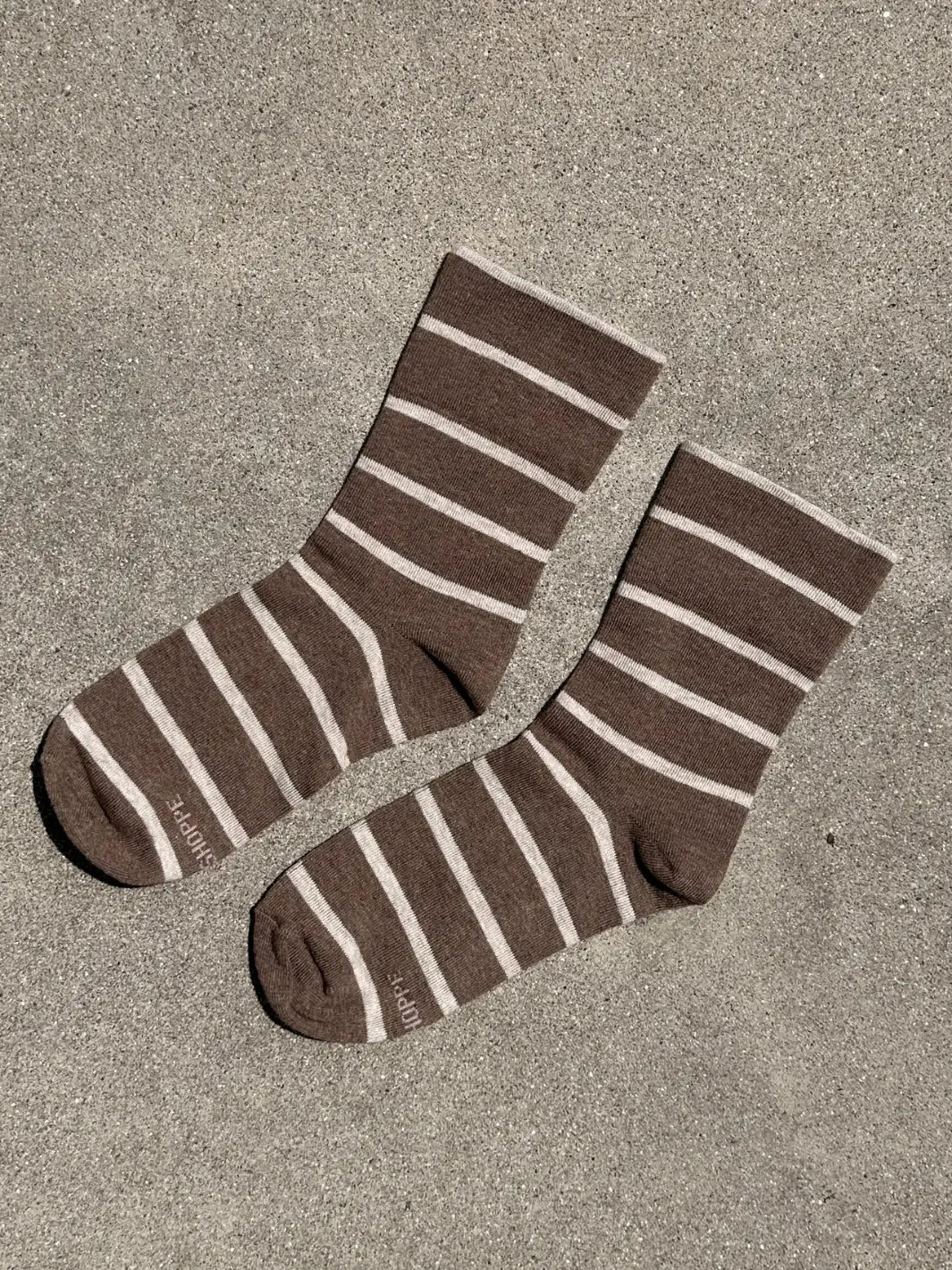 A pair of brown and cream striped Wally Socks in Mocha from Le Bon Shoppe is displayed flat on a textured concrete surface | Twentyseven Toronto