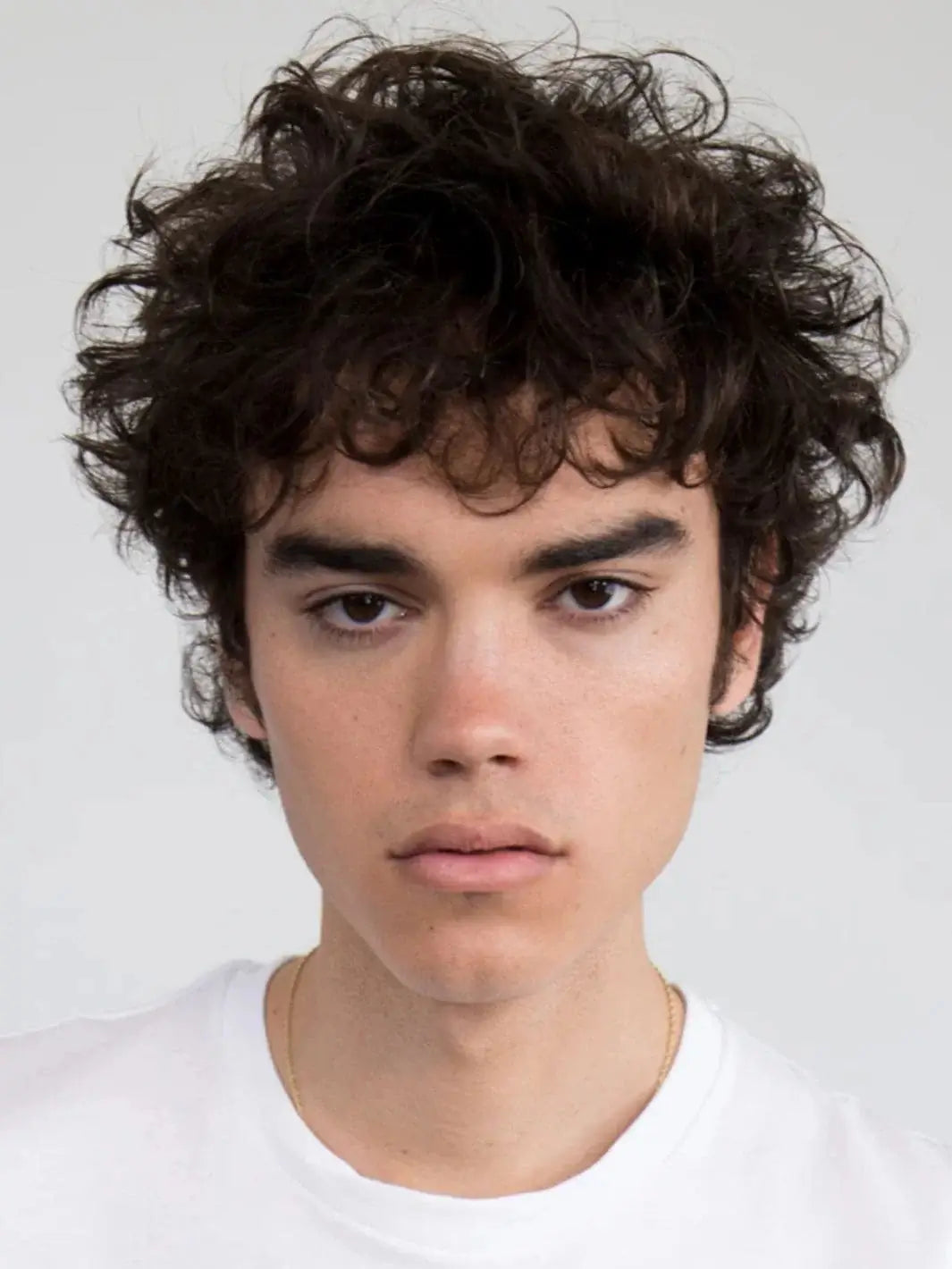 A model with textured, dark curly hair showcases defined shine and moisture after styling with R+Co WATERFALL Moisture + Shine Lotion | Twentyseven Toronto