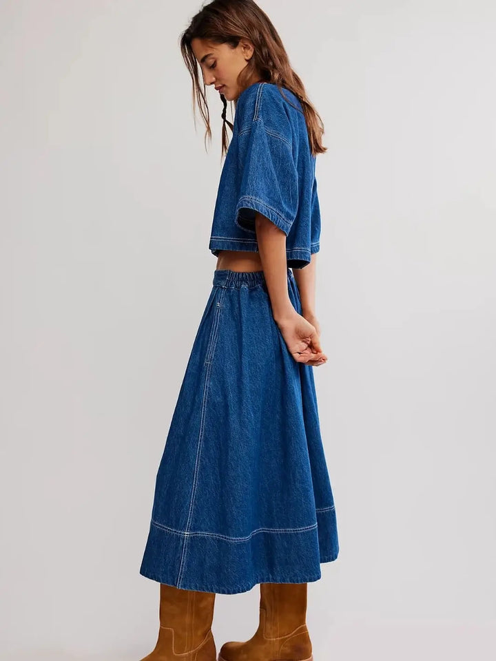A side profile view showcases the relaxed fit, wide short sleeves, and midi length of the Free People Westley Denim Skirt Set in Deep Sea Wash paired with brown suede boots | Twentyseven Toronto