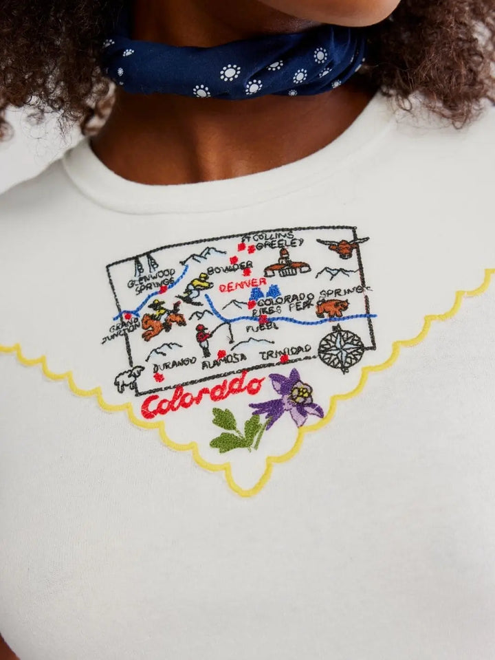 A detailed close-up focuses on the intricate, multi-colored embroidered Colorado map graphic and yellow scalloped border on the chest of the Free People Wild Country Tee - Colorado Combo | Twentyseven Toronto