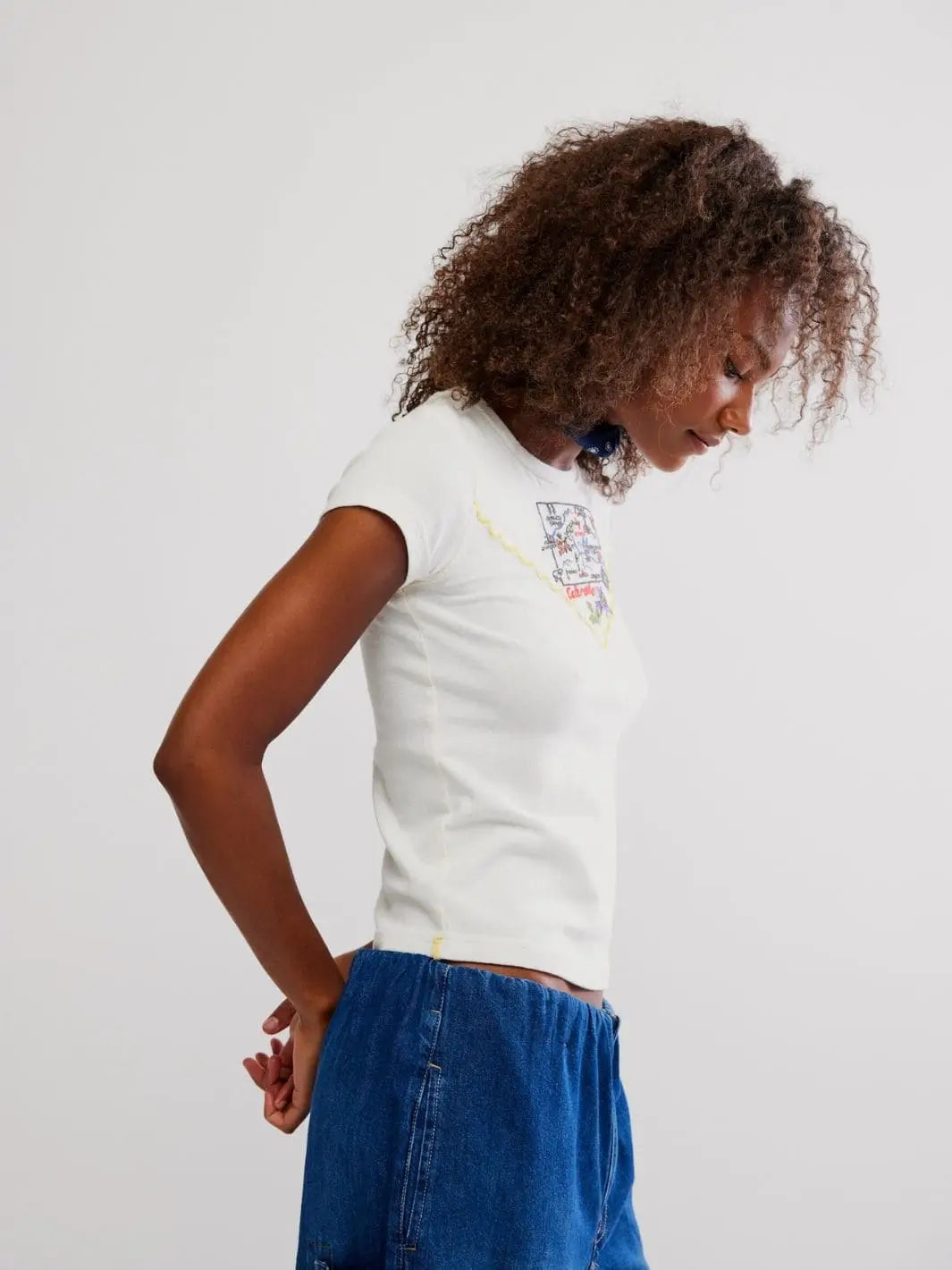 A side profile view highlights the short capped sleeves and contouring fit of the white Free People Wild Country Tee - Colorado Combo paired with blue denim | Twentyseven Toronto
