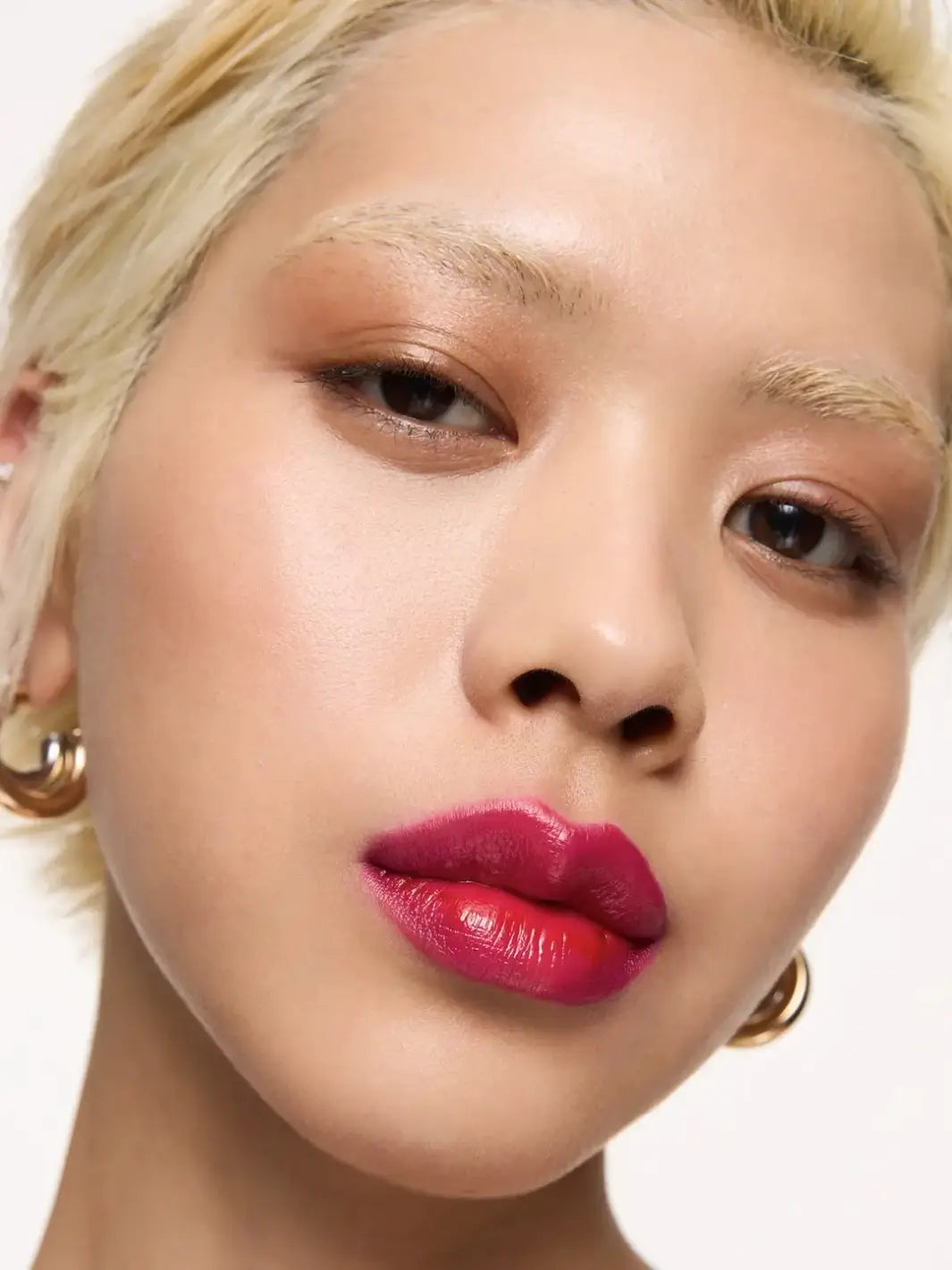 A close-up of a fair-skinned model with short blonde hair showcasing a vibrant magenta lip color from the Wonderskin WONDER BLADING Lip Stain Masque in Neon Rose | Twentyseven Toronto