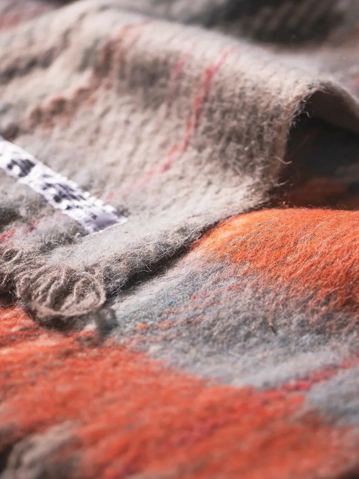 Close-up of the Puebco Recycled Wool Mix Blanket, highlighting its textured wool-blend fabric, soft grey and orange plaid pattern and fringed edges. | Twentyseven Toronto