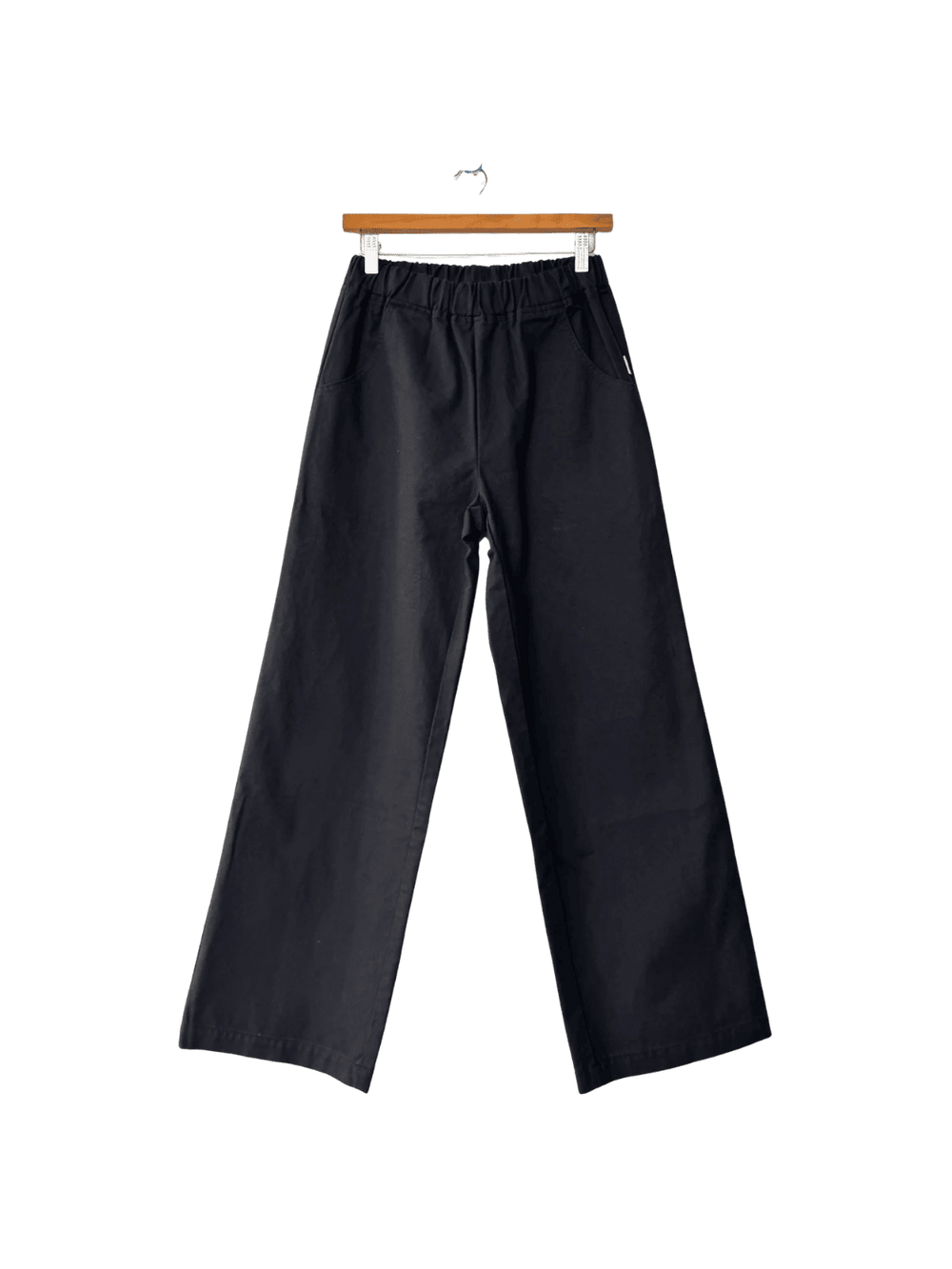 Black Le Bon Shoppe 'Work Pants' hanging on a wooden hanger against a transparent background | Twentyseven Toronto