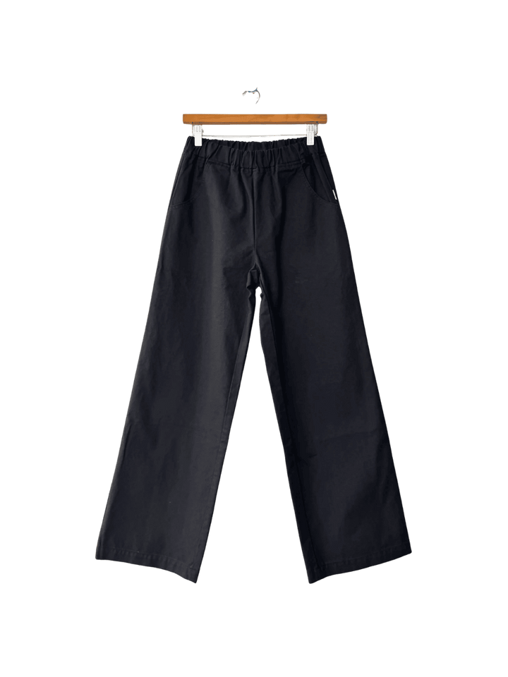 Black Le Bon Shoppe 'Work Pants' hanging on a wooden hanger against a transparent background | Twentyseven Toronto