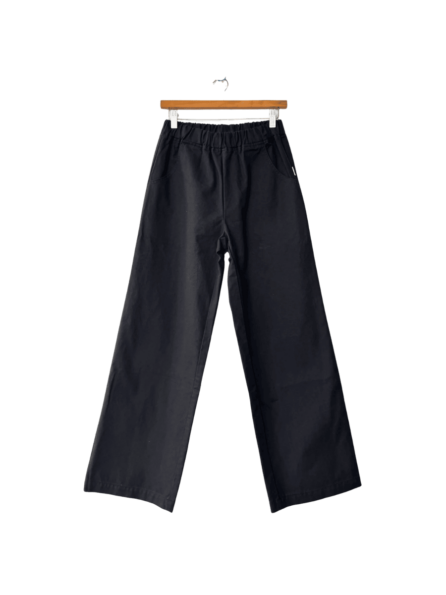 Black Le Bon Shoppe 'Work Pants' hanging on a wooden hanger against a transparent background | Twentyseven Toronto