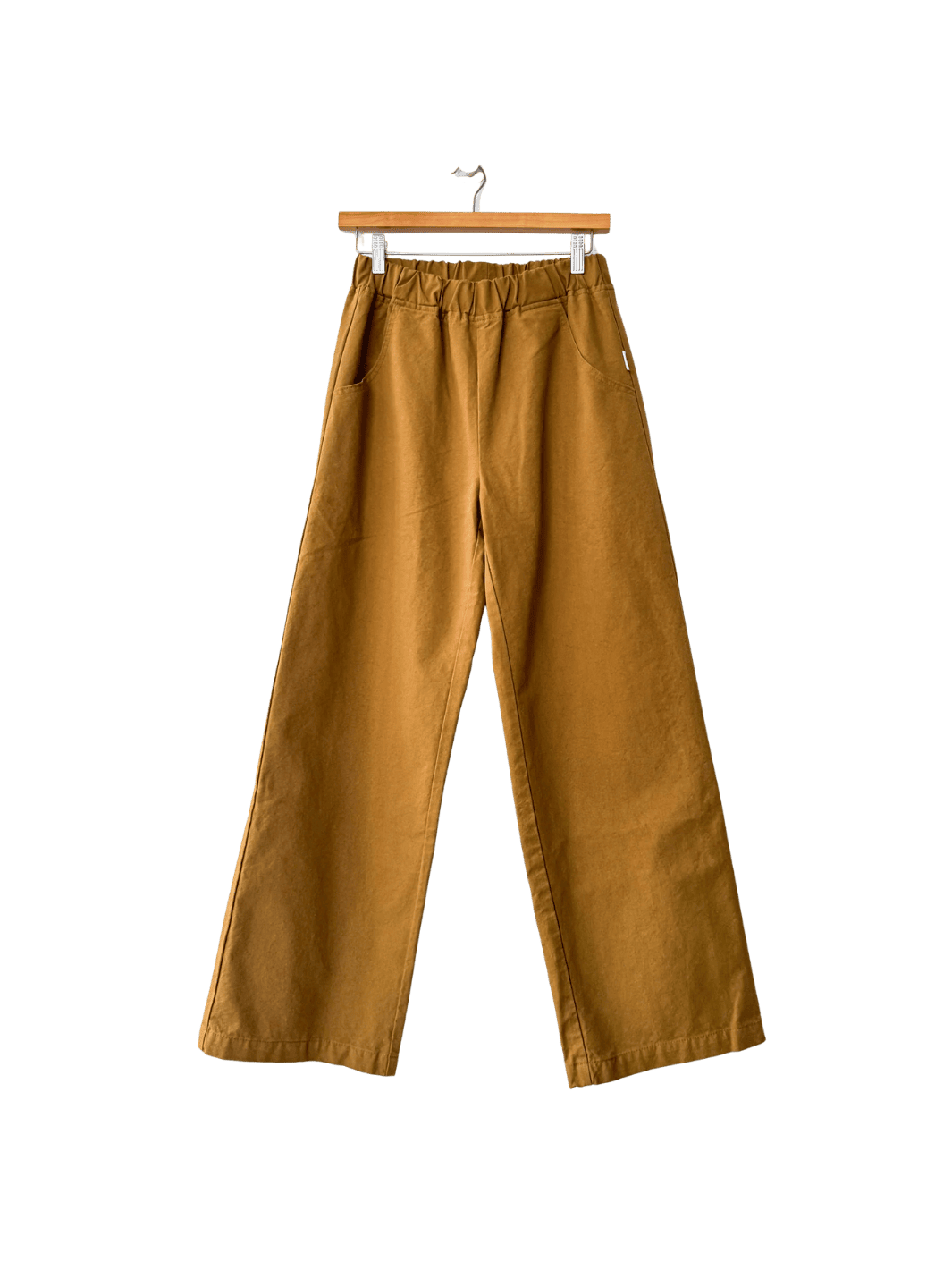 Mustard yellow Le Bon Shoppe 'Work Pants' in 'Dijon' hanging on a wooden hanger against a transparent background | Twentyseven Toronto