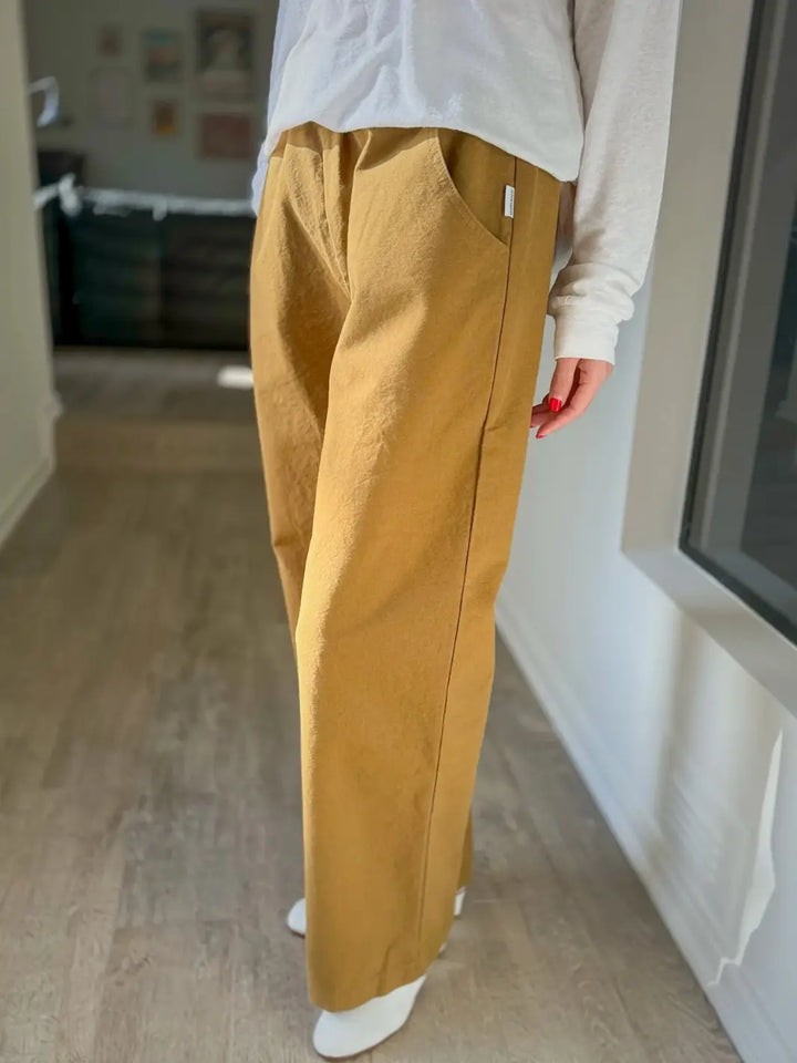 Side view of person wearing mustard yellow 'Work Pants' in 'Dijon' and a white top from Le Bon Shoppe indoors | Twentyseven Toronto