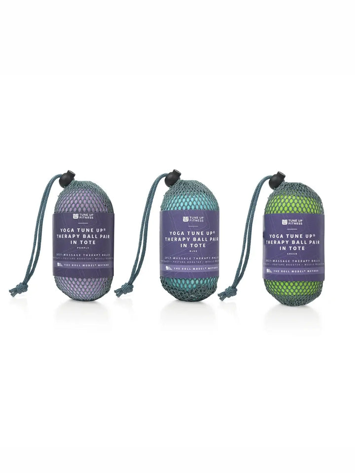 Three mesh bags holding a pair therapy balls from Tune Up Fitness, one in purple, one in blue and one in green with label on a white background | Twentyseven Toronto