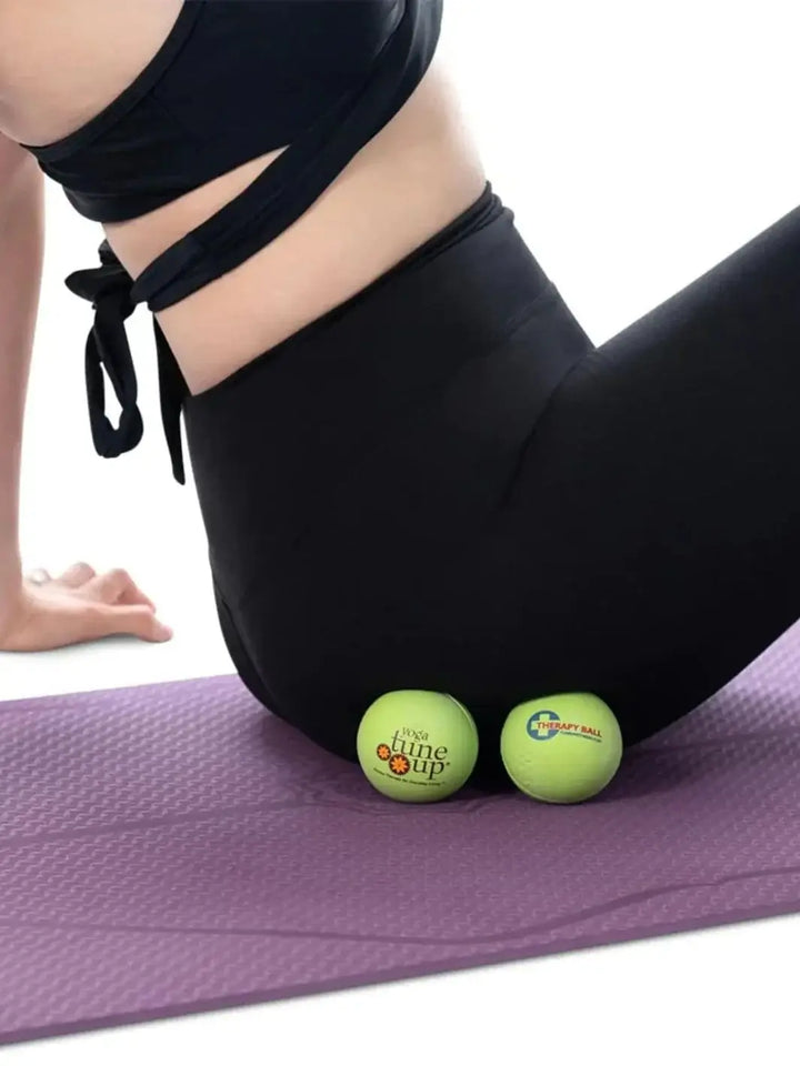 Person using two green Tune Up Fitness therapy massage balls on a purple yoga mat | Twentyseven Toronto