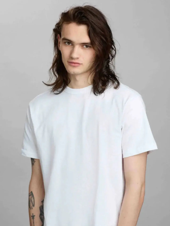 A model with shoulder-length, textured brown hair poses against a grey background, showcasing a look styled with R+Co ZIPPER Multitasking Styling Lotion | Twentyseven Toronto